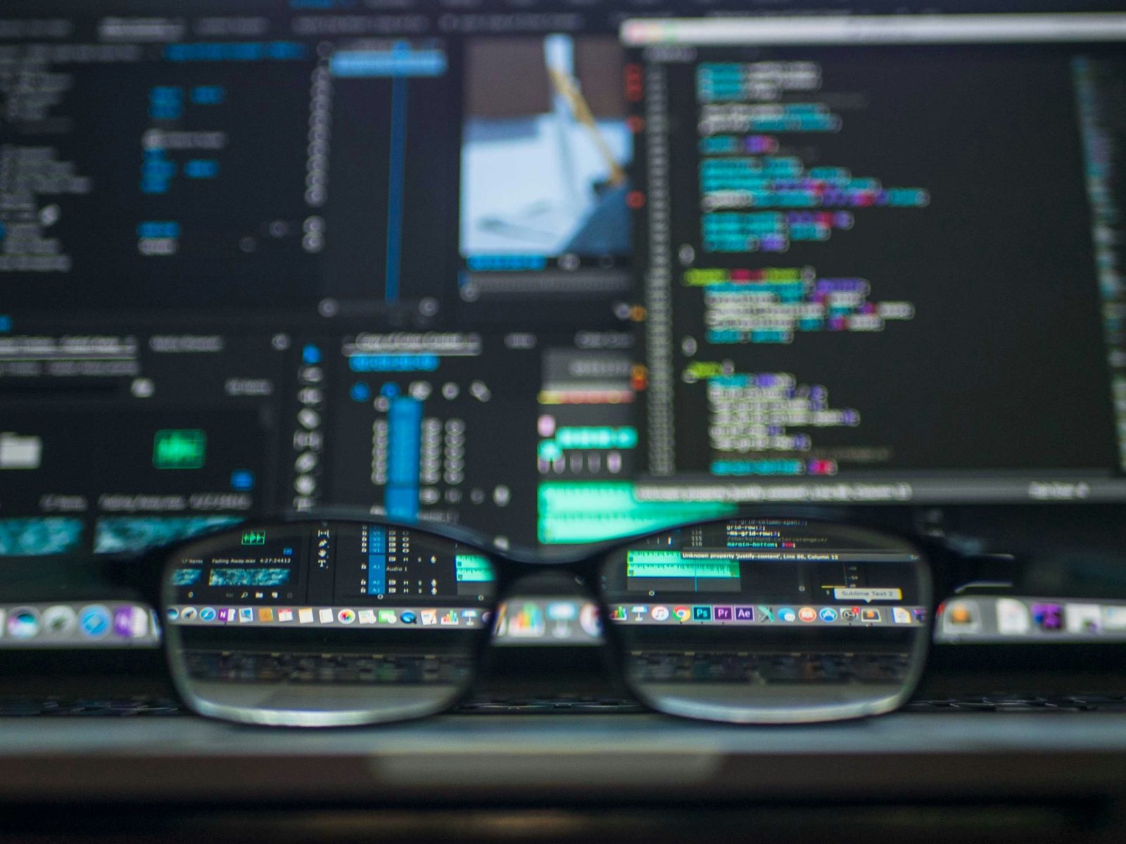 Glasses in focus in front of blurred monitors showing code and data