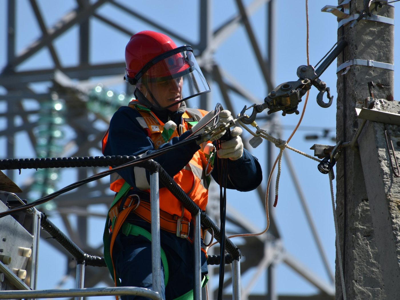 Lineworker in a red helmet and face shield working from a bucket lift on high-voltage equipment