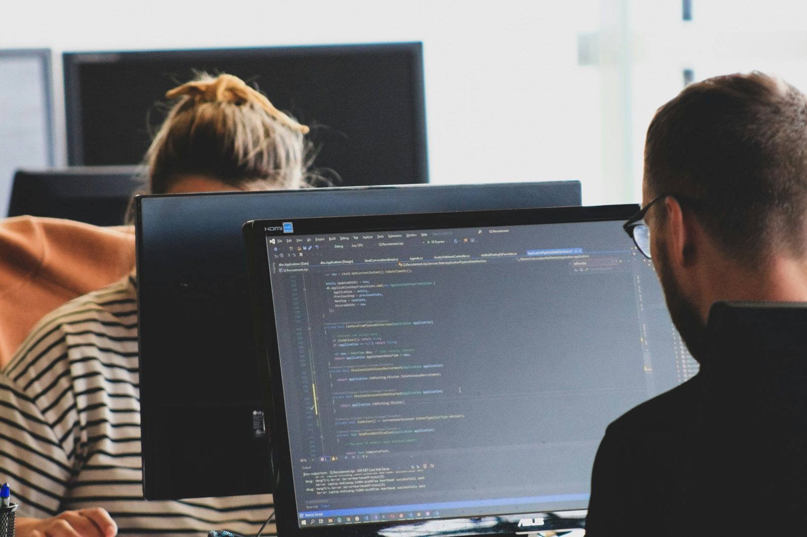Two analysts at their workstations, one reviewing code on a monitor